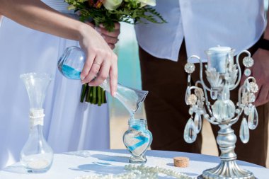 Gelin ve damat kristal vazoya renkli kumlar döküyor. Sembolik deniz dekoru merasimi sırasında okyanusun önündeki kumlu kumsalda evlilik birleşme töreni sırasında kapatılıyor. 