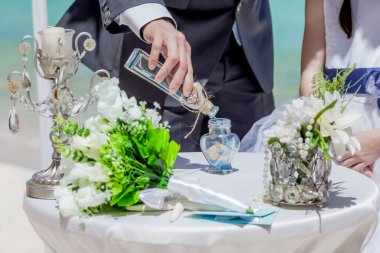 Gelin ve damat kristal vazoya renkli kumlar döküyor. Sembolik deniz dekoru merasimi sırasında okyanusun önündeki kumlu kumsalda evlilik birleşme töreni sırasında kapatılıyor. 