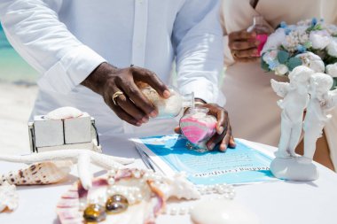 Gelin ve damat farklı renklerde kumları kristal vazonun içine döküyor. Sembolik deniz dekoru merasimi sırasında okyanusun önündeki kumlu kumsalda nikah töreninde yakın durun. 