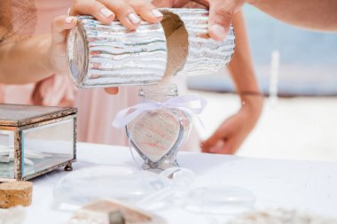 Gelin ve damat farklı renklerde kumları kristal vazonun içine döküyor. Sembolik deniz dekoru merasimi sırasında okyanusun önündeki kumlu kumsalda nikah töreninde yakın durun. 