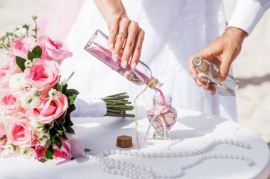 Gelin ve damat farklı renklerde kumları kristal vazonun içine döküyor. Sembolik deniz dekoru merasimi sırasında okyanusun önündeki kumlu kumsalda nikah töreninde yakın durun. 
