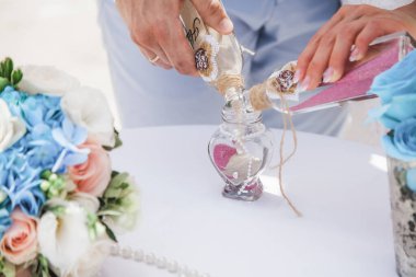 Gelin ve damat farklı renklerde kumları kristal vazonun içine döküyor. Sembolik deniz dekoru merasimi sırasında okyanusun önündeki kumlu kumsalda nikah töreninde yakın durun. 