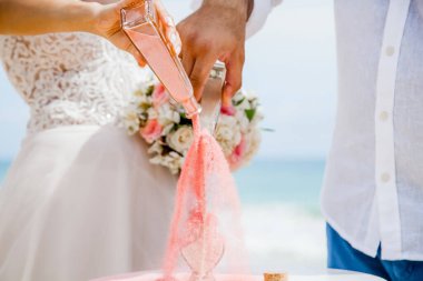 Gelin ve damat farklı renklerde kumları kristal vazonun içine döküyor. Sembolik deniz dekoru merasimi sırasında okyanusun önündeki kumlu kumsalda nikah töreninde yakın durun. 