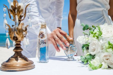 Gelin ve damat farklı renklerde kumları kristal vazonun içine döküyor. Sembolik deniz dekoru merasimi sırasında okyanusun önündeki kumlu kumsalda nikah töreninde yakın durun. 