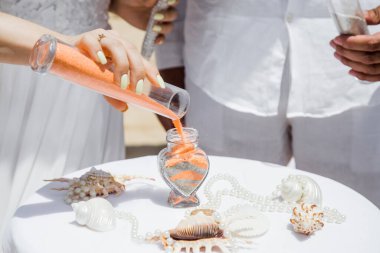 Gelin ve damat farklı renklerde kumları kristal vazonun içine döküyor. Sembolik deniz dekoru merasimi sırasında okyanusun önündeki kumlu kumsalda nikah töreninde yakın durun. 