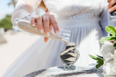 Gelin ve damat farklı renklerde kumları kristal vazonun içine döküyor. Sembolik deniz dekoru merasimi sırasında okyanusun önündeki kumlu kumsalda nikah töreninde yakın durun. 