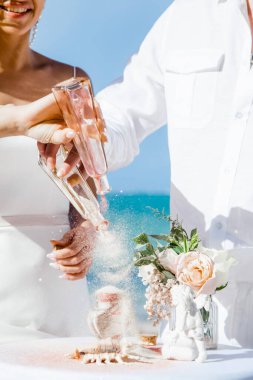 Gelin ve damat farklı renklerde kumları kristal vazonun içine döküyor. Sembolik deniz dekoru merasimi sırasında okyanusun önündeki kumlu kumsalda nikah töreninde yakın durun. 