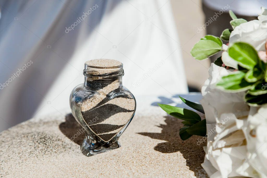 Bride and groom pouring colorful different colored sands into the crystal vase close up during symbolic nautical decor destination wedding marriage ceremony on sandy beach in front of the ocean 