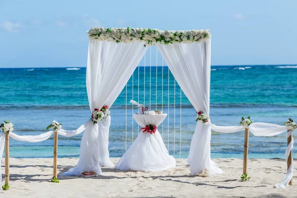 Colorful wedding arch gazebo pavilion made of bamboo and textile with fresh flowers decoration at sandy beach on sunny day for destination wedding ceremony in Dominican republic
