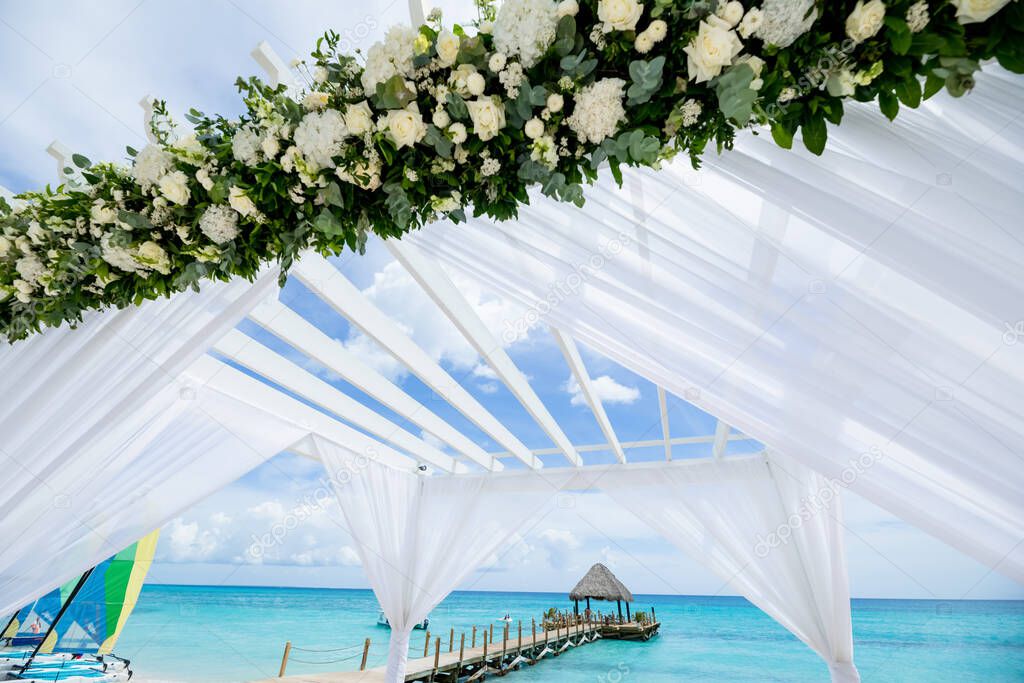 Colorful wedding arch gazebo pavilion made of bamboo and textile with fresh flowers decoration at sandy beach on sunny day for destination wedding ceremony in Dominican republic  