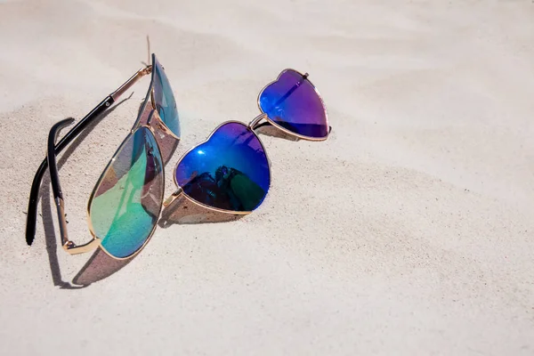 Pair on sunglasses laying on the sand on sunny day. Male and female sunglasses. Heart shaped glasses. Vacation concept. Vacations on tropical island, unity concept