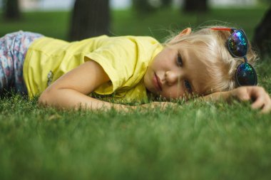 Kız güneş gözlüğü ve sarı tişört çim üzerinde yalan