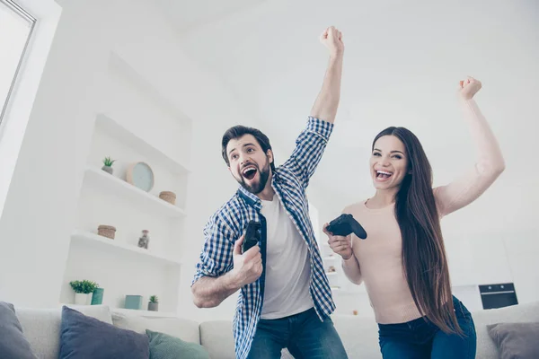 Goal! Portrait of cheerful positive couple enjoying victory in videogame on playstation jumping with raised fists, screaming, holding console, gamepad in hands, fans of x-box