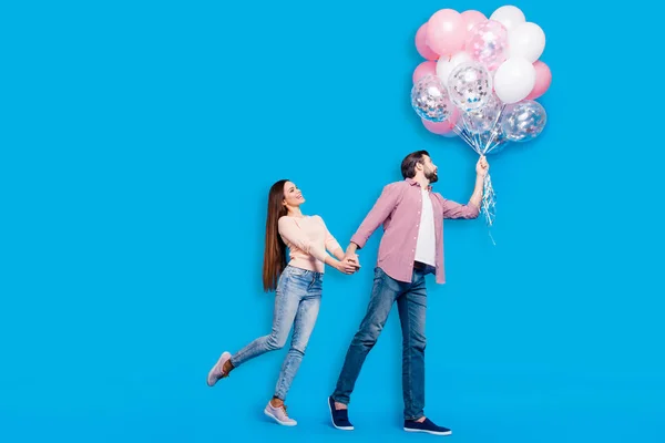 Full size body portrait of funny comic partners in jeans sneakers casual outfits having many air balloons isolated on blue background. Love story concept