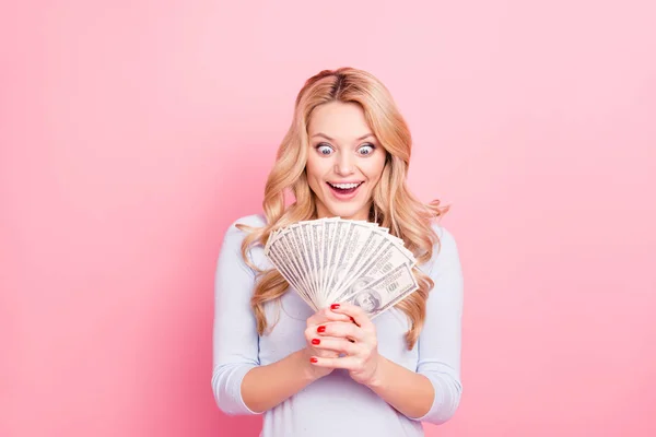 Portrait of astonished surprised crazy girl with wide open eyes, mouth looking at much money in her hands, isolated on pink background. Jack-pot, casino player concept