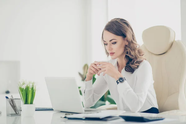 漂亮的女人与现代的发型在白色衬衫看着笔记本电脑屏幕 看电影视频有杯茶在手坐在工作地点站 — 图库照片