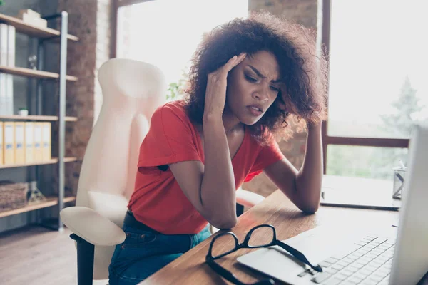 Portrait of sad upset woman feeling bad unwell with unhappy emotions holding hands on temples suffering from head ache sitting at desk. Health care concept