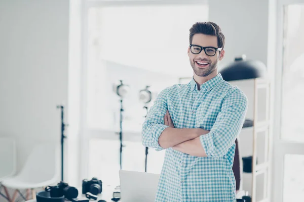 Portrait of attractive cheerful photo camera lover standing in  photo studio with crossed arms, laughing at camera, his hobby to shoot nice photo sessions