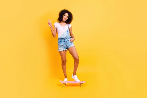 全体的に黄色の背景で隔離のポケットなめんま保持ハンド ジェスチャー スケート ボードに乗ってデニムで穏やかなフレンドリーな女の子の全身肖像画 運動の極端なバランスの活動の概念 — ストック写真