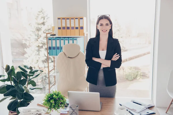 开朗时尚的女人手持双手交叉穿着夹克裙眼镜头上看着相机站在桌面上与供应在现代办公室的肖像 — 图库照片