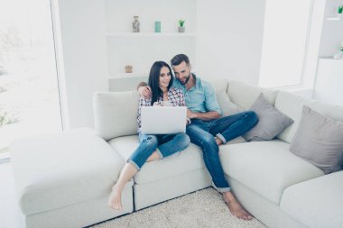 Social networks film movie video online meeting connection communication concept. Full size portrait of lovely couple enjoying online purchase  using wi-fi internet sitting in modern white livingroom clipart
