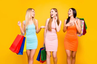 Center mall showroom package commerce black friday concept. Portrait of slim funky girls going from boutique holding many bags in hands sharing comic funny gossips isolated on bright yellow background clipart