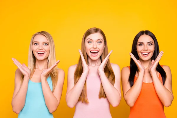 Great! Portrait of amazed pleased trio holding palms near face having good news information isolated on vivid yellow background