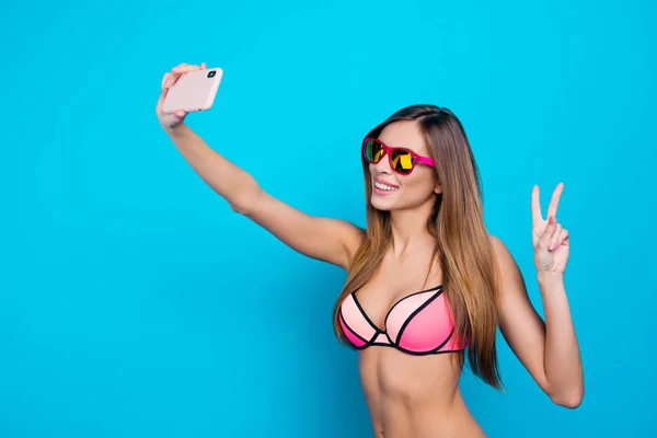 水泳でフレンドリーな創造的な女の子の肖像画を着用する青い背景に分離されたフロント カメラで Selfie を撮影 本の指を手でジェスチャーのスマート フォンを持っていること — ストック写真