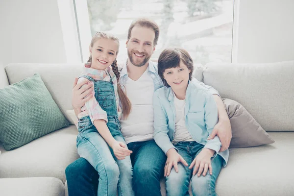 Portrait of family with one parent, positive joyful father embracing two kids sitting indoor on sofa wearing casual outfit enjoying free time together. Understanding upbringing concept
