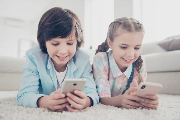 Retrato Dos Niños Tumbados Estómago Alfombra Piso Sosteniendo Teléfonos Inteligentes —  Fotos de Stock