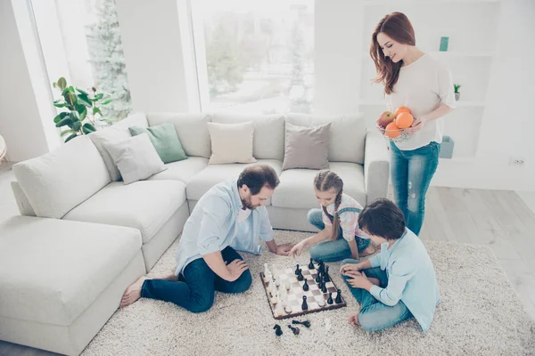画像的父亲和两个孩子玩象棋棋盘游戏规划策略坐在沙发附近的地毯上 微笑的妈妈带水果的游戏玩家 田园概念 — 图库照片