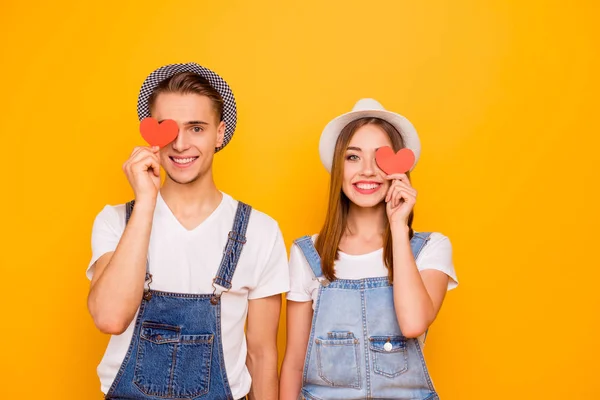 年轻快乐的学生夫妇在爱戴着帽子抱着两个小红纸心的眼睛 — 图库照片