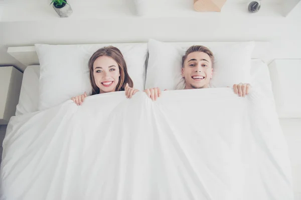 年轻迷人的昏昏欲睡的情侣的肖像在床上醒来 在早晨 覆盖着毯子 女孩和男人微笑着他们的牙齿 上方高角度视图 — 图库照片