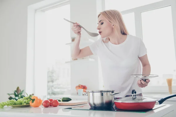 可爱迷人的成人迷人的女人穿着睡衣白色 T恤烹调品尝食物从罐子用勺子红色蕃茄绿色沙拉碎黄瓜黄色胡椒粉躺在白色的餐桌上 — 图库照片