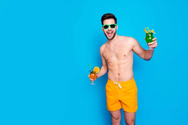 ビーチ スタイル 黄色のショート パンツと 眼鏡で魅力的な陽気な男は青い背景に分離の手で小さな傘でカクテルを保持します うれしそうな暑い夏の概念 — ストック写真