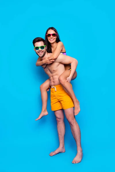 在蓝色背景下被隔离的夏日旅行者的全长肖像 快乐的情侣 眼镜上的男人和黄色的短裤背着带背的快乐女人 深色头发 看着相机 — 图库照片