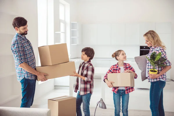 Young happy smiling family four persons unpacking carton packages with stuff in light kitchen, moving to new house