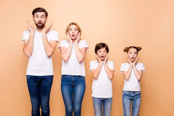 Portrait of young surprised family, bearded father, blonde mother and their little children wearing jeans and white T-shirts, standing straight and gesturing unsurely placing palms to cheeks — Stock Image Portrait Young Surprised Family Bearded Father Blonde Mother Little Children Stock Picture