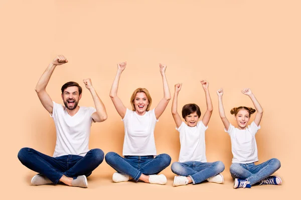 Young smiling family, bearded father, blonde mother, little boy and girl wearing blue jeans and white T-shirts, sitting in odrer of hierarchy in lotus pose raising up hands — Stock Image Young Smiling Family Bearded Father Blonde Mother Little Boy Girl Stock Picture