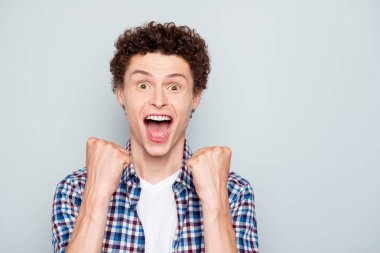 We make it! Close up portrait of stylish happy young guy with hands clasped in fists and loud yell in happiness isolated on light gray background with copy space for text clipart