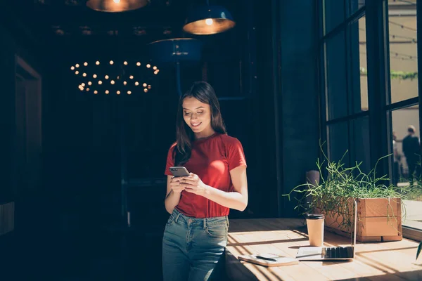 Молодая очаровательная девушка стоит с кафе со смартфоном в руках — стоковое фото