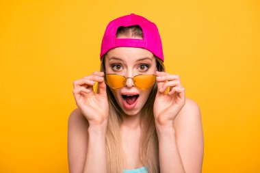 Summer discounts for travel! Close up portrait of shocked and surprised girl looks at the camera over glasses with wide-open eyes and mouth isolated on shine yellow background clipart