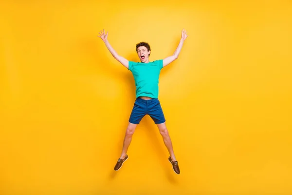全尺寸长身体图片英俊的卷发滑稽的年轻人穿着休闲绿色 T恤衫 跳跃在空气中 手向上 明星人物 在黄色背景下隔离 — 图库照片