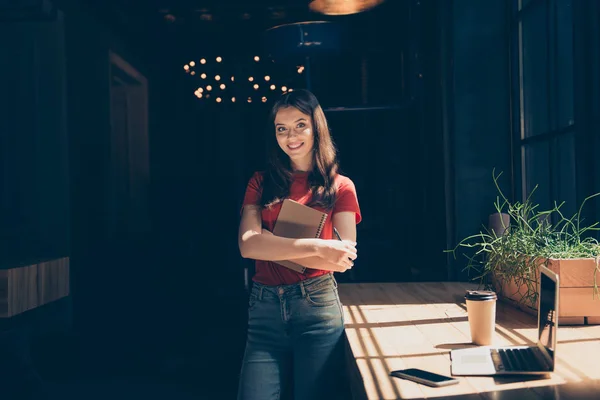 迷人的漂亮的微笑的年轻女孩自由职业者的学生穿着休闲在自助餐厅 远程工作 持有纸垫 深色内饰 — 图库照片