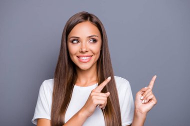 Portrait of brown-haired gorgeous attractive nice smiling young lady with logn hair over grey background, showing pointing up and side with fingers, isolated, copy space clipart