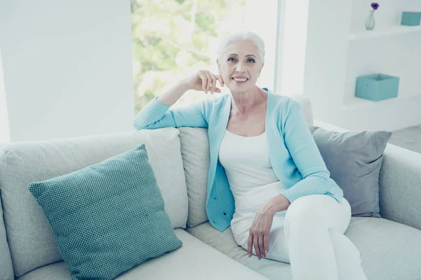 Encantadora anciana sentada en un sofá en la sala de estar y mirando — Foto de Stock