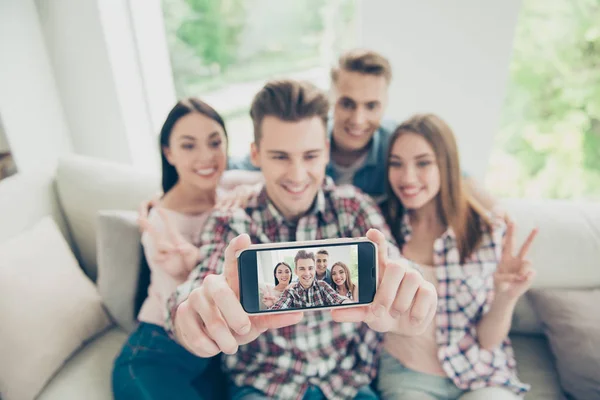 Toda la atención al teléfono inteligente Enfoque en la pantalla del teléfono moderno con un fondo borroso con cuatro jóvenes tomar selfie sentado en un sofá en ropa de mezclilla —  Fotos de Stock
