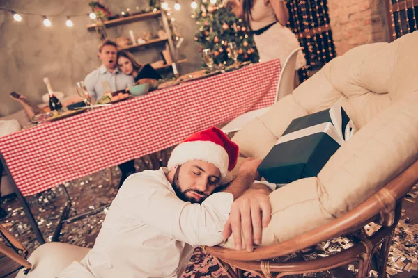 Barbu gars dans santa claus cap dormir sur le sol, chaise près de gif — Photo