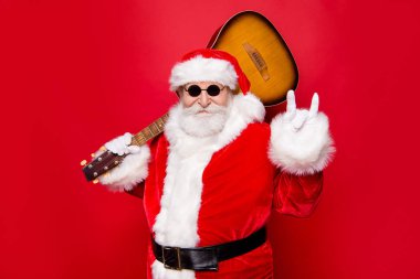 Christmastime December concept. Aged fancy stylish grandfather Nicholas in costume white beard show rock n roll sign hold guitar on shoulder ready playing song sound isolated on red background clipart