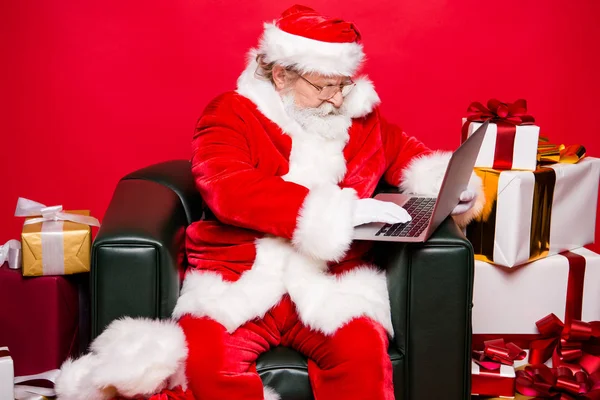 圣诞冬天12月前夕诺埃尔 侧面视图老年聚焦集中阅读器祖父圣诞老人白胡子坐在扶手椅看屏幕希望发送接收电子邮件隔离红色背景 — 图库照片